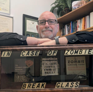 The author doug burbey leaning on a case that says break in case of zombies with a sword in it.